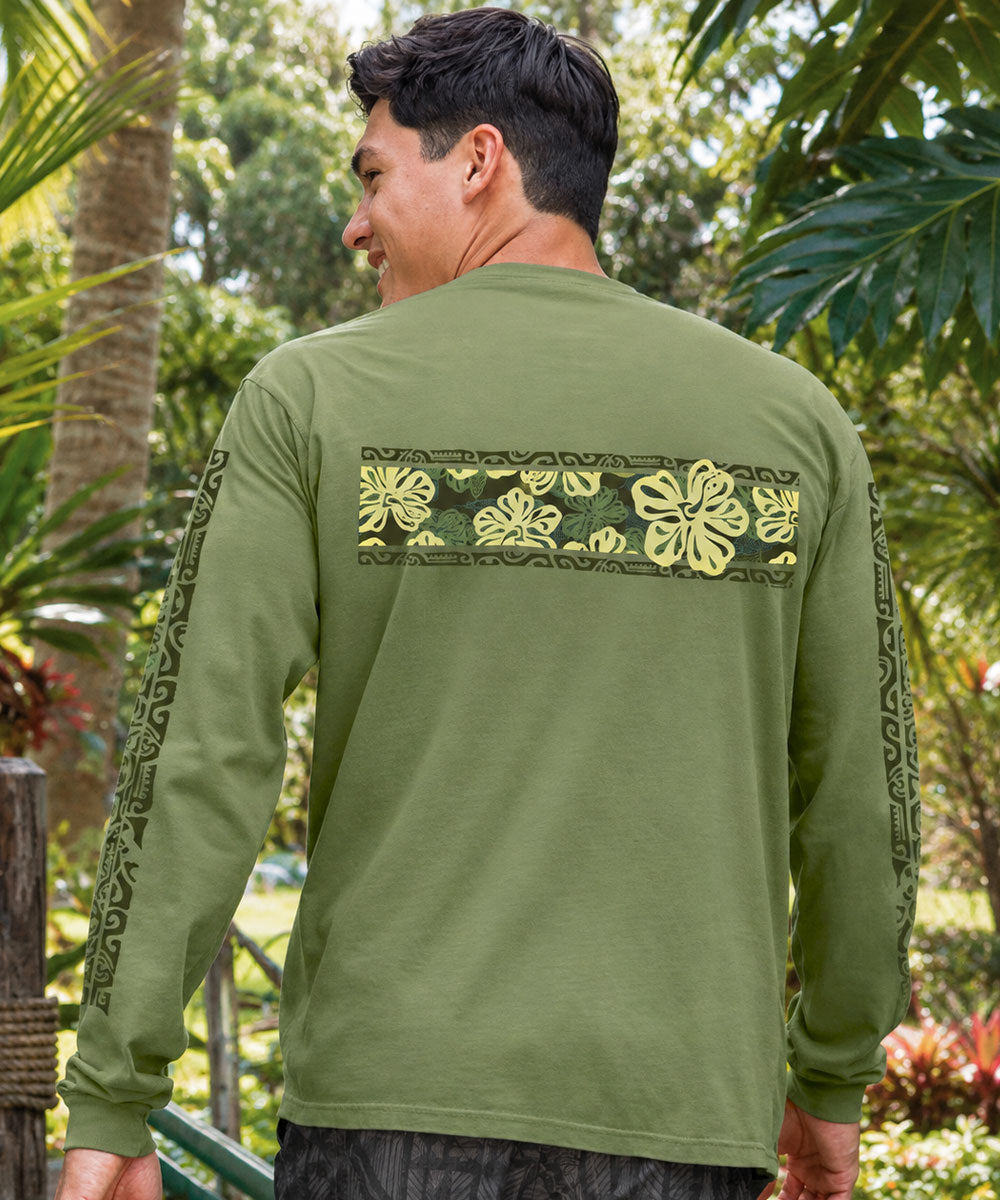 A man wearing an olive green long-sleeve shirt with a yellow and black floral pattern across the back and down the sleeves, photographed outdoors in a tropical garden setting. View 3