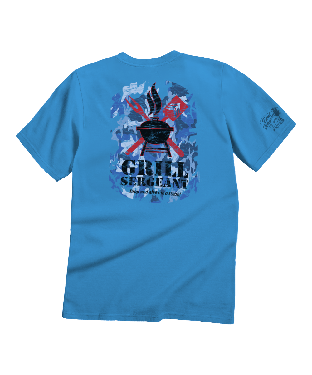 A bright blue short-sleeve t-shirt shown from the back, featuring a large graphic print with a grill, flames, crossed red and blue elements, and the text 'GRILL SERGEANT' with smaller text below. A smaller graphic is printed on the left sleeve. View 1