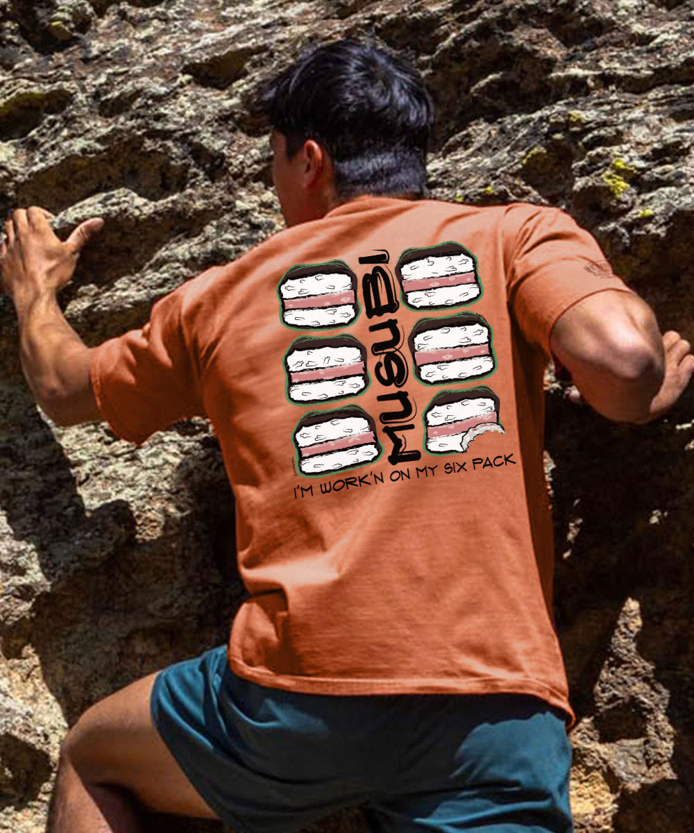 A man climbing a rocky outcrop, viewed from behind, wearing an orange crewneck t-shirt with a sushi-themed back graphic and the brand name 'iGuren' printed vertically. View 2