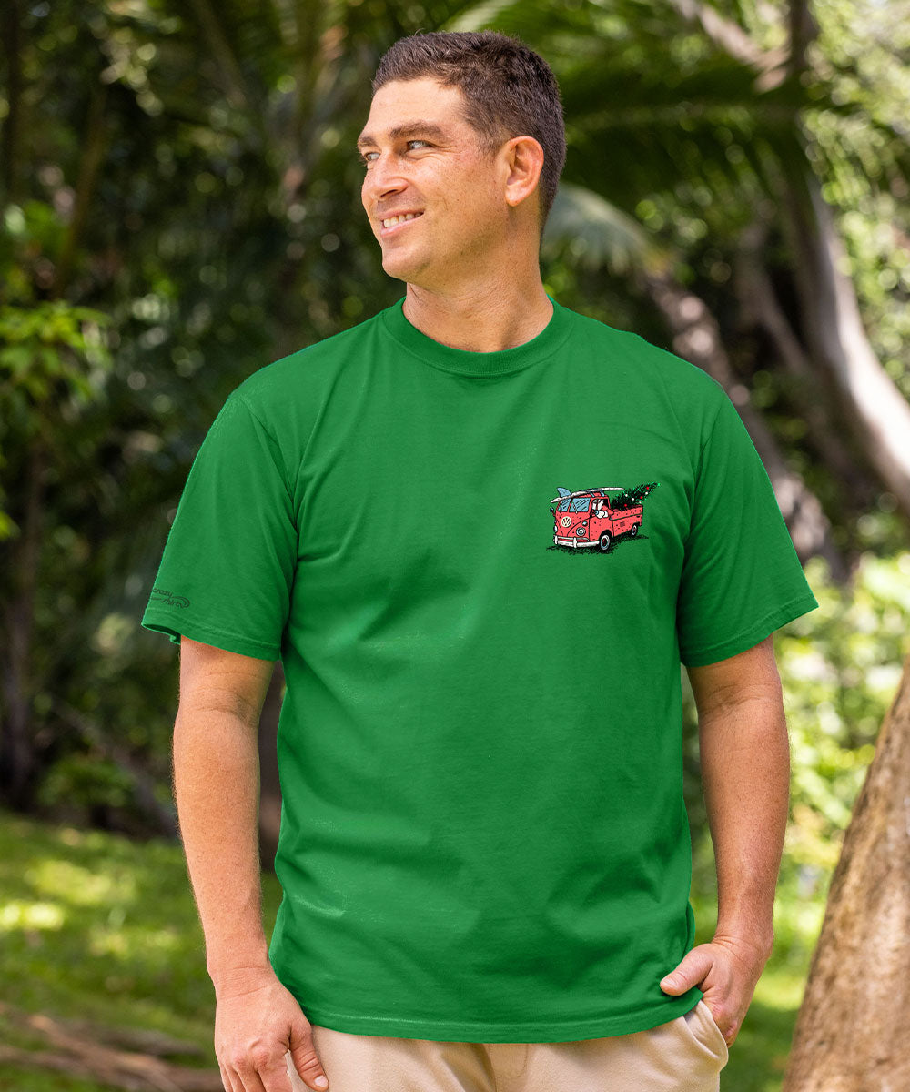 A man wearing a bright green crewneck t-shirt with a small red fire truck graphic on the left chest, standing outdoors in a lush green environment. View 3