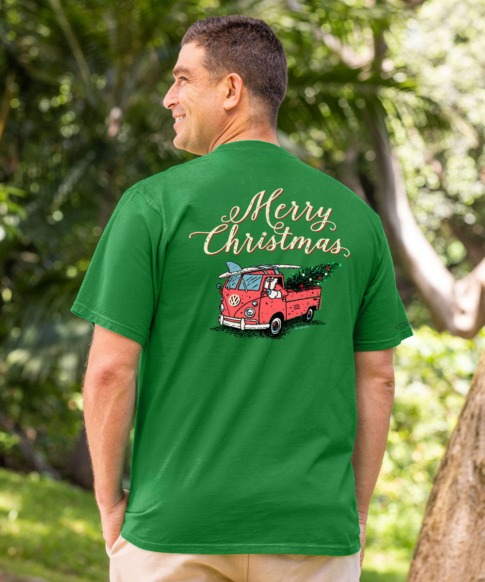 A man wearing a green t-shirt with a 'Merry Christmas' graphic on the back, standing outdoors in a park with trees in the background. View 2