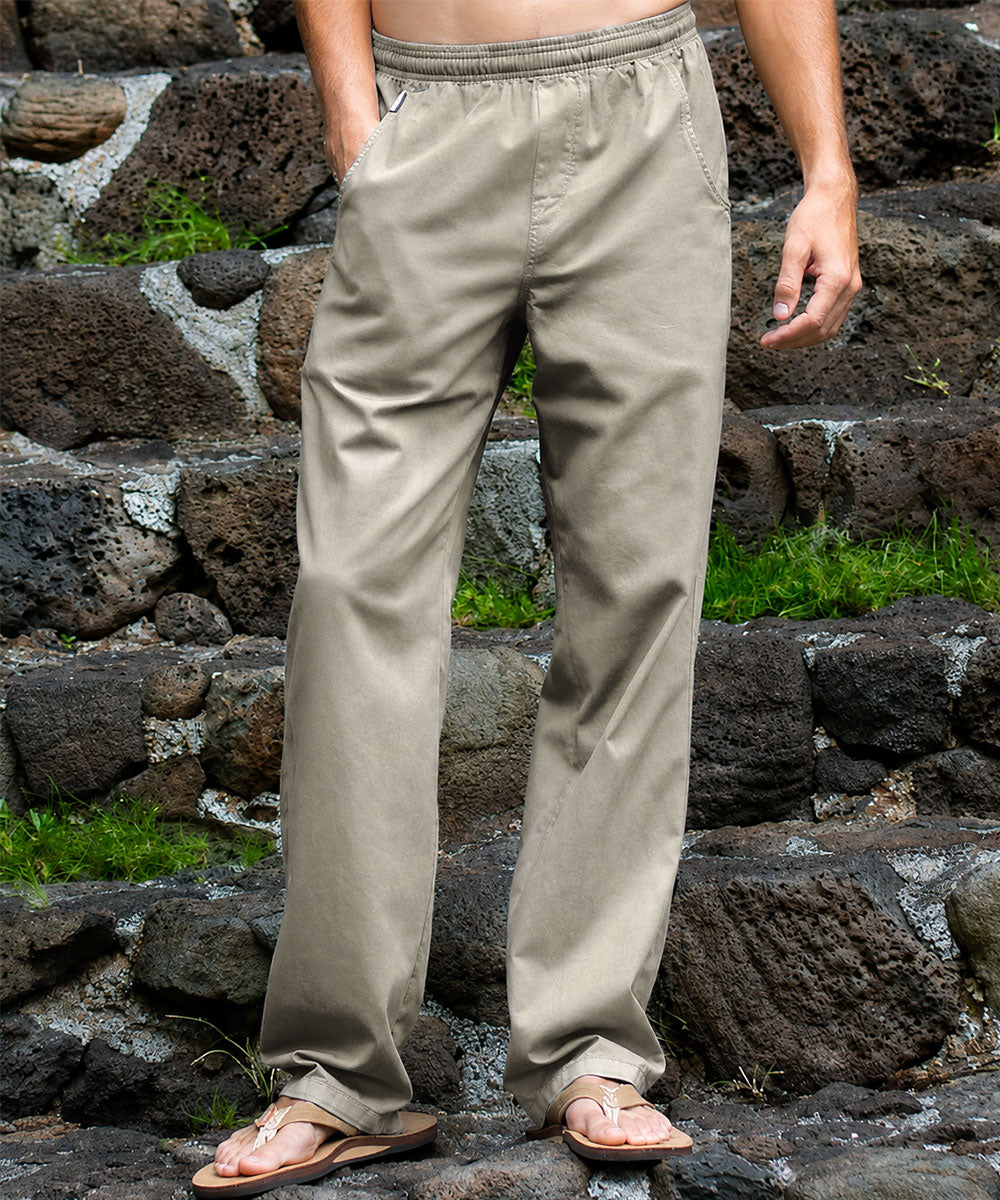 A person wearing light beige drawstring pants and tan sandals, standing on dark volcanic stone steps with green moss in the background. View 2