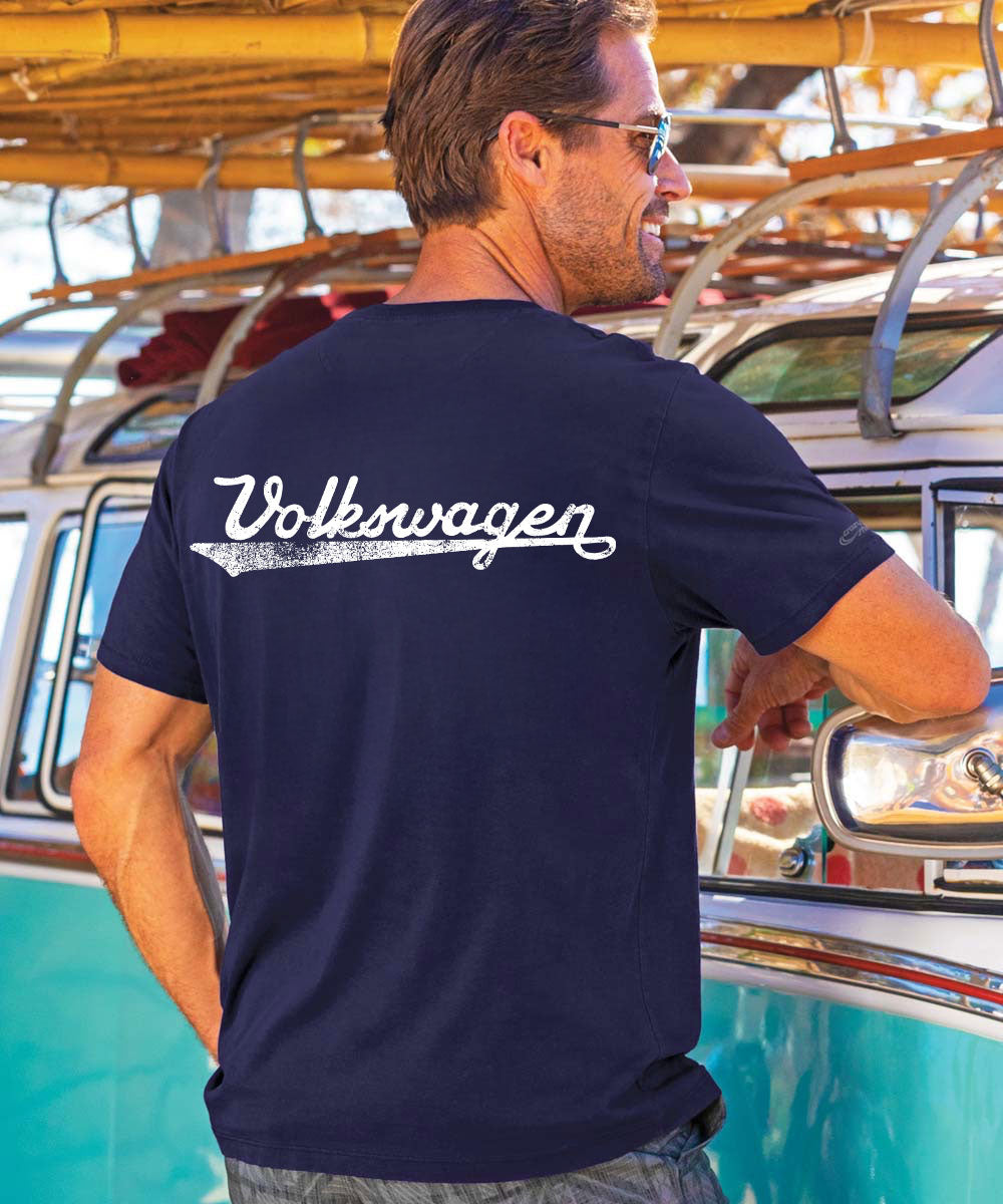 Man wearing a navy Volkswagen t-shirt standing next to a vintage turquoise van. View 3