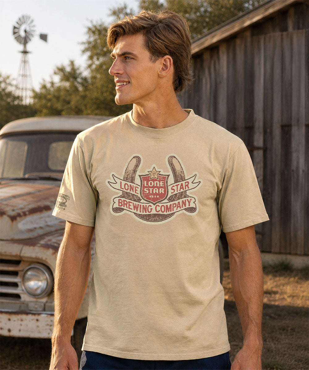 Man wearing a beige t-shirt with a 'Lone Star Brewing Company' logo on a beach. View 2