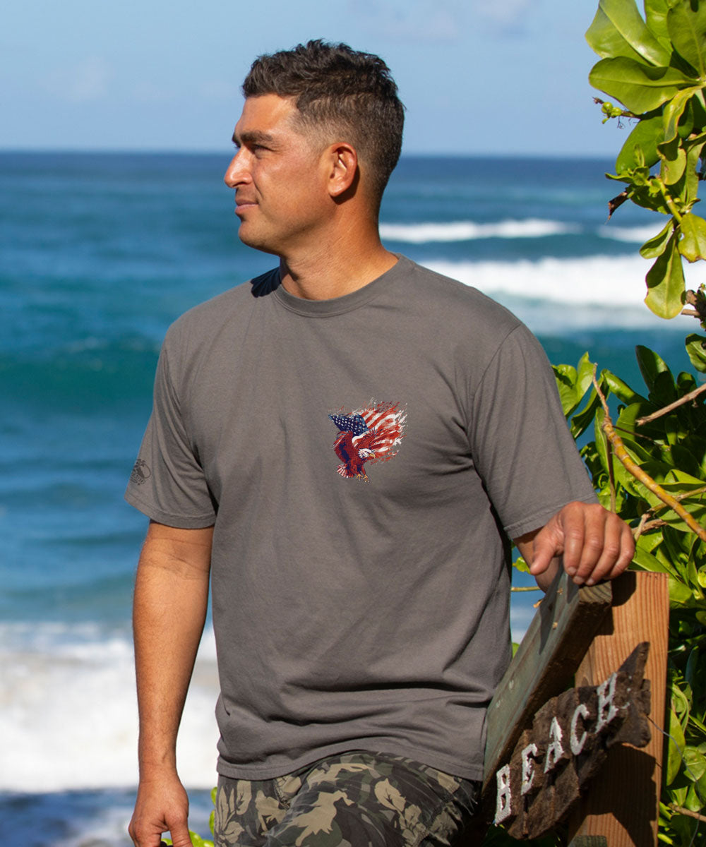 Man wearing a gray t-shirt with a logo standing by the ocean View 3