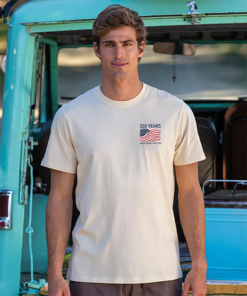 Man wearing a white t-shirt with a graphic design in front of a turquoise vehicle. View 3