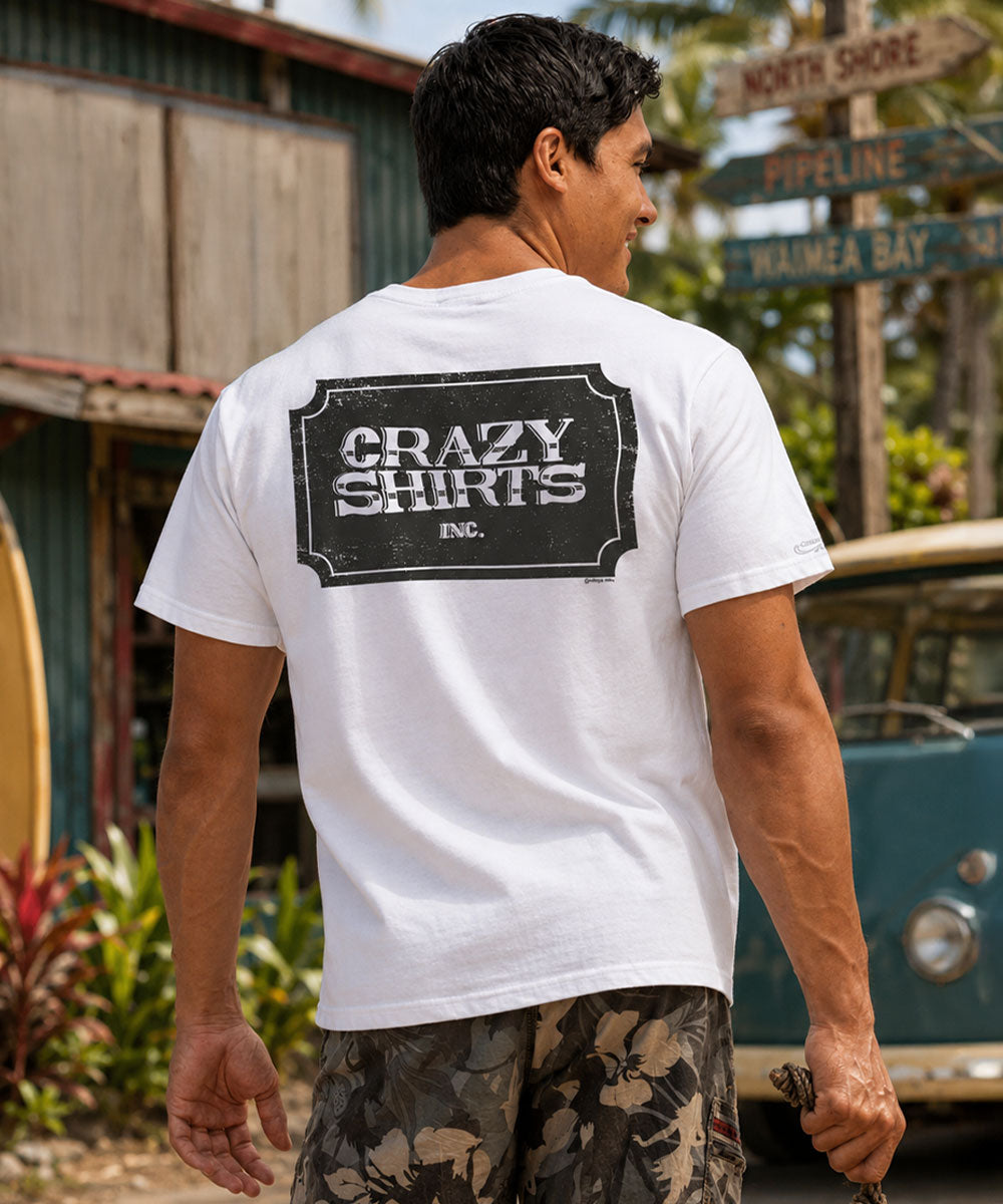 Man wearing a white t-shirt with 'Crazy Shirts Inc.' on the beach