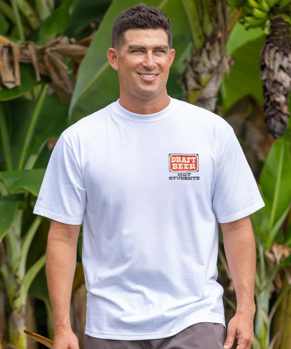 Man wearing a white t-shirt with a logo and text, standing in front of green foliage. View 3