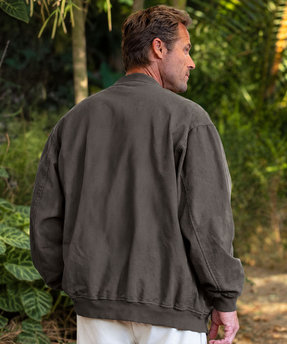 A man viewed from behind wearing an oversized dark gray jacket, standing in front of foliage View 3