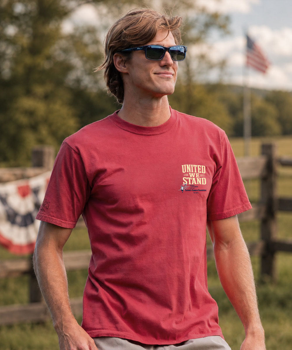 A man wearing a red crewneck t-shirt with a yellow 'UNITED WE STAND' graphic on the left chest, photographed outdoors  View 3