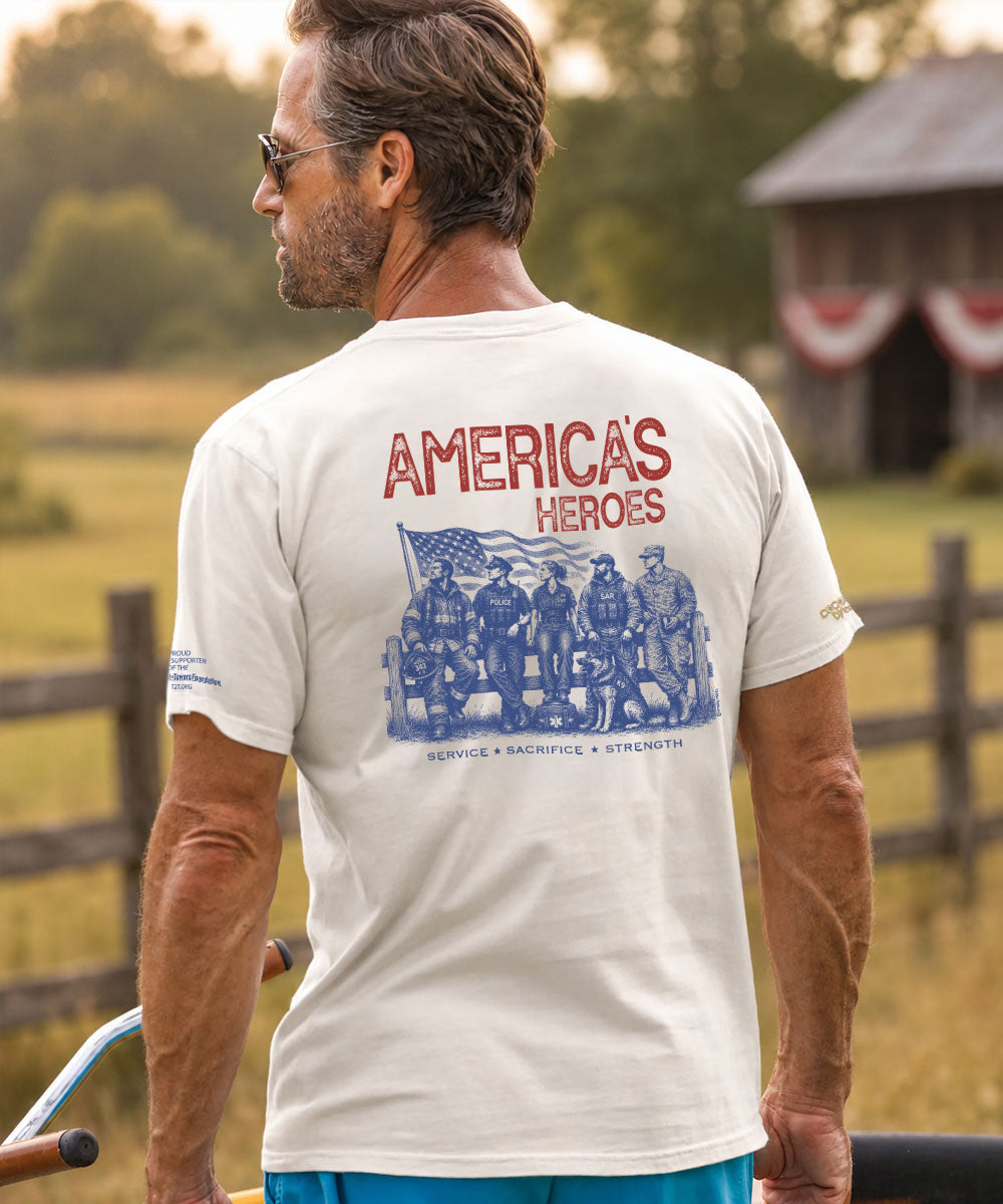 A man wearing a cream-colored t-shirt with a blue and red graphic on the back, standing outdoors on a farm. View 2