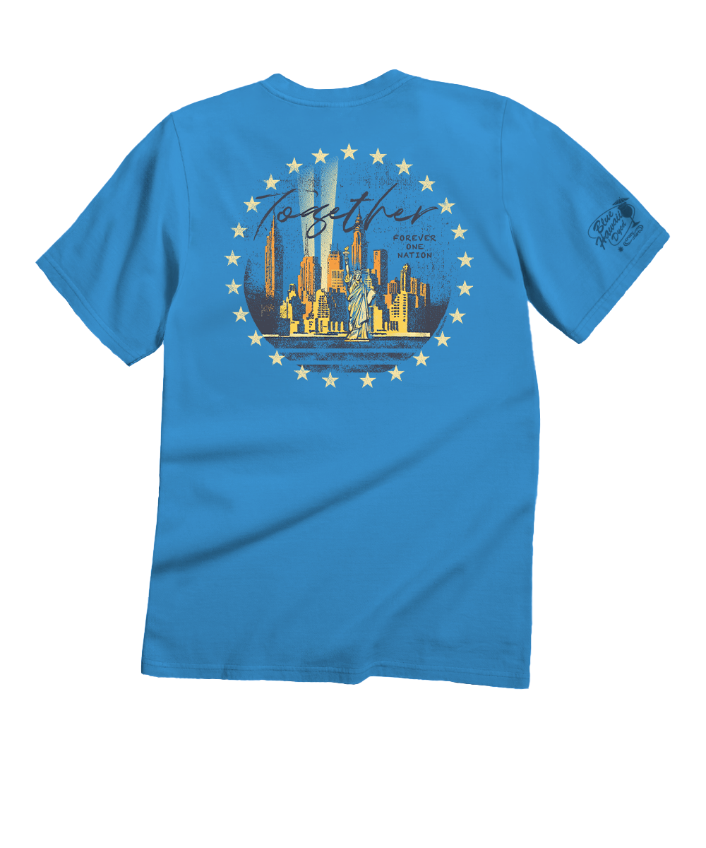 A bright blue short-sleeve t-shirt shown from the back, featuring a large graphic print of the New York City skyline with the Statue of Liberty and the word 'Together' in script, surrounded by a circle of stars. A smaller graphic is printed on the left sleeve. View 1