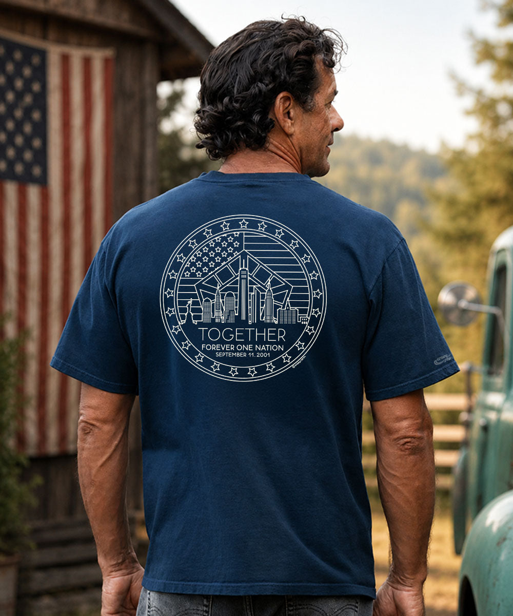 A man viewed from behind wearing a navy blue t-shirt with a large white circular graphic on the back. The graphic features a city skyline, the American flag, and the text 'TOGETHER' and 'FOREVER ONE NATION'. View 2