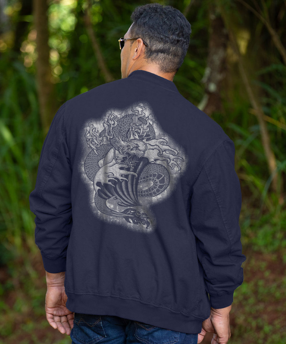 A man viewed from behind wearing a navy blue jacket with a large gray and white graphic print of a sea creature and wave design on the back, set against a blurred green forest background. View 2