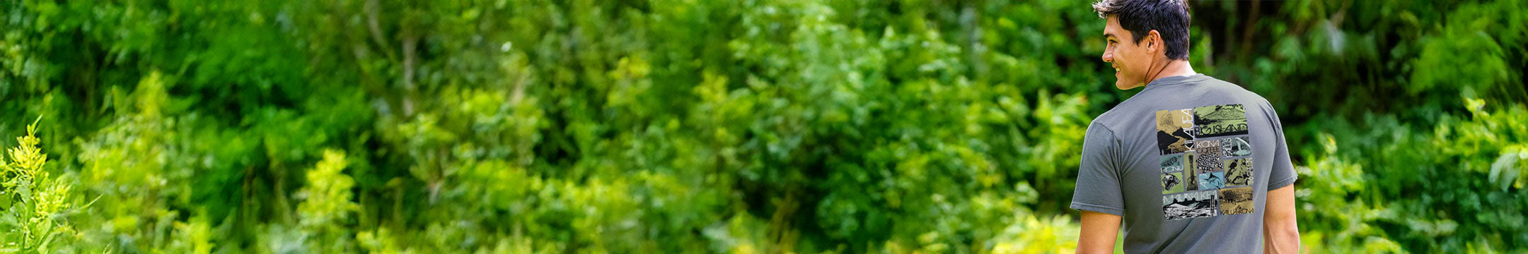 Man walking through a forest wearing a gray t-shirt with a graphic design.