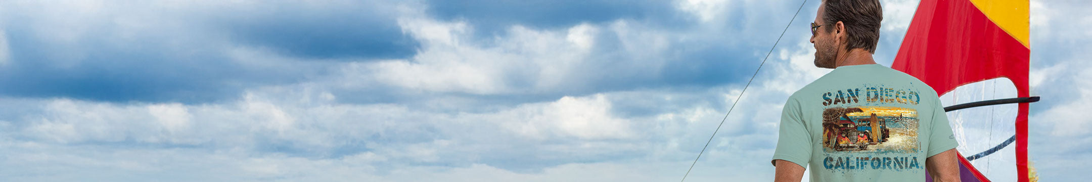 Man wearing a 'San Diego, California' t-shirt with a scenic design, standing against a cloudy sky.