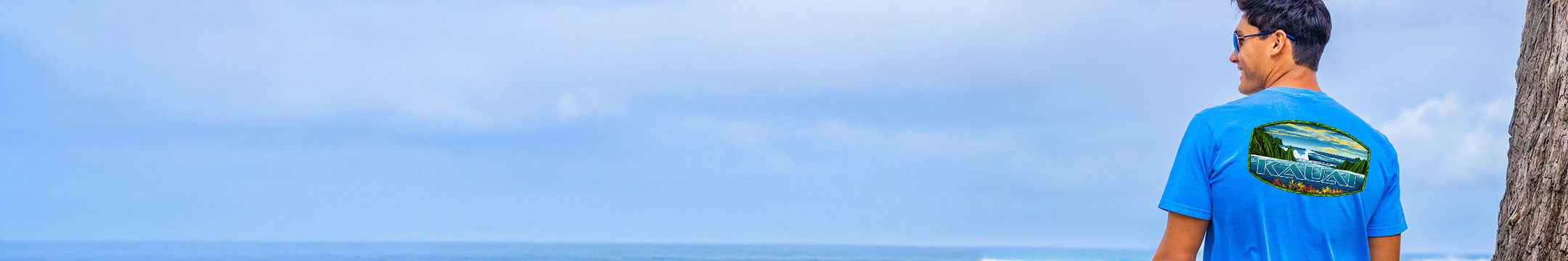 Man wearing a blue t-shirt with a graphic design, standing against a clear blue sky.