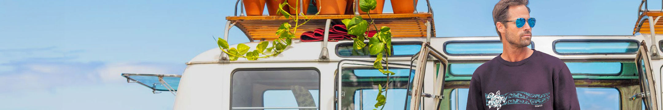 Man standing next to a van with plants on top, wearing sunglasses and a dark shirt.