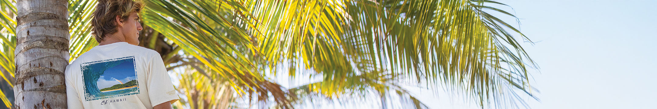 Man wearing a crazy shirt tee leaning against a palm tree