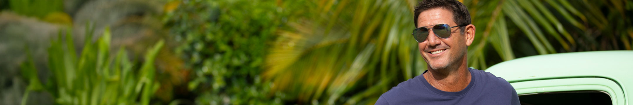 Man wearing sunglasses and a blue shirt standing in front of green foliage