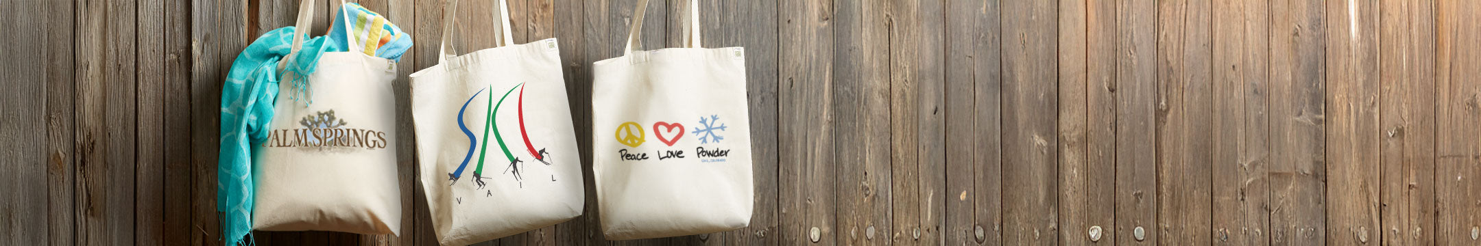 Three tote bags with printed designs on a wooden surface