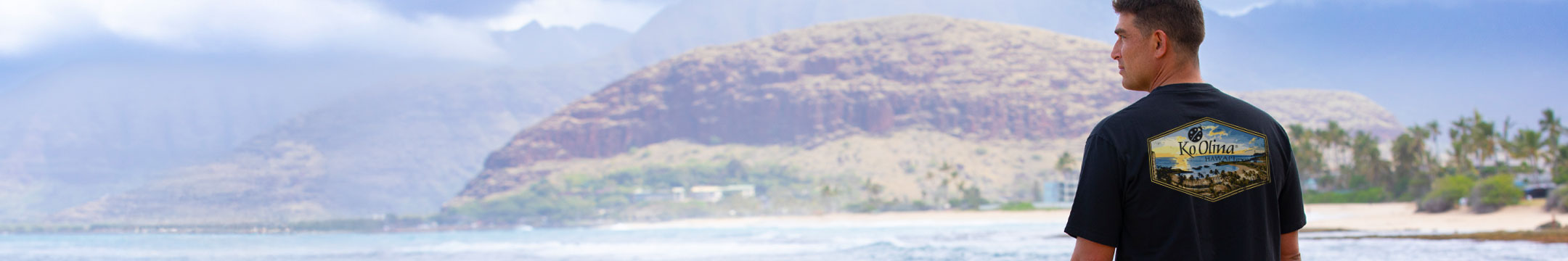 Man wearing a black short sleeve tee shirt standing on a beach looking into the distance.