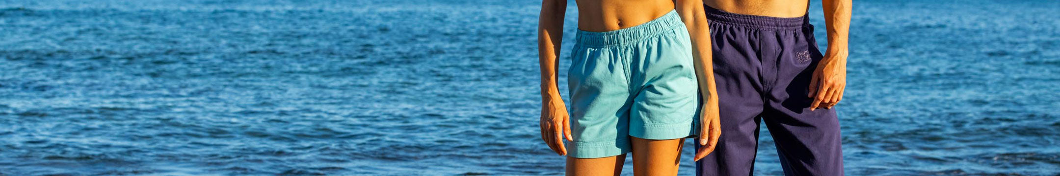 Two people standing by the water wearing Crazy Shirts shorts and pants 