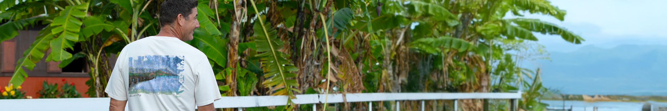 Man standing by a white railing with lush greenery and a house in the background