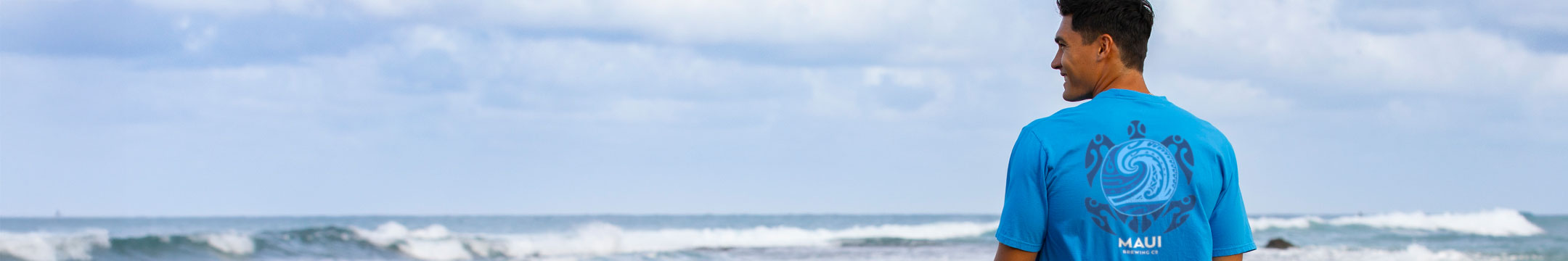 Man on the beach looking into the distance wearing a blue shirt