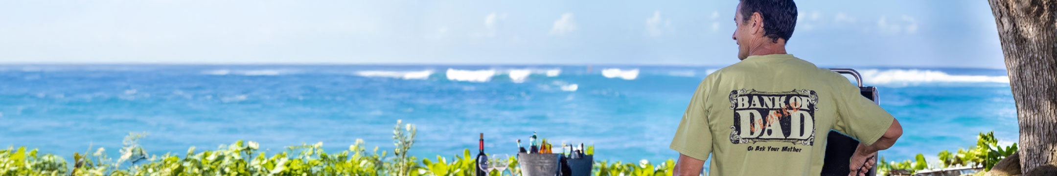 Man in a green shirt with 'Dad' printed on it standing by the ocean.