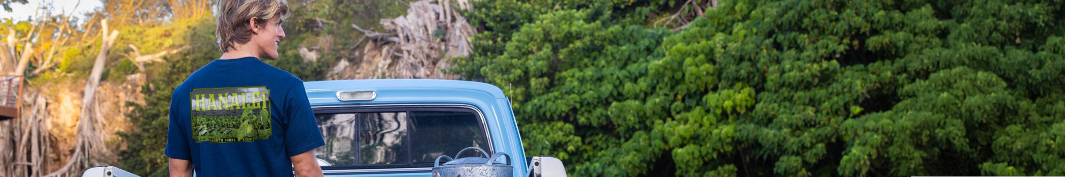 Person wearing a t-shirt with text standing next to a vintage truck in a forest setting