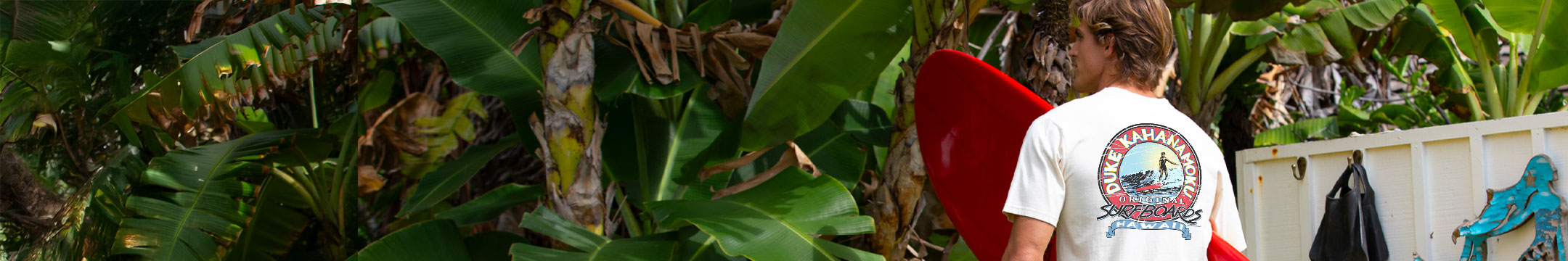 man in front of greenery wearing a tan shirt holding a surfboard.