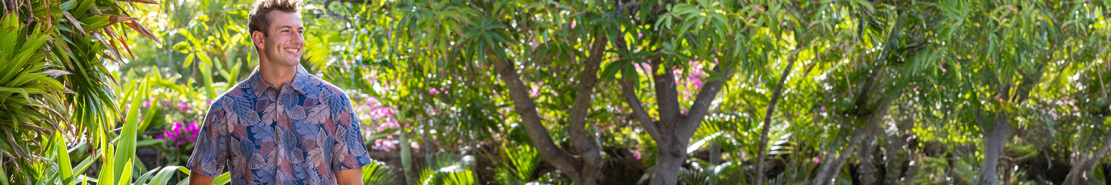 Man in a patterned shirt standing among lush greenery