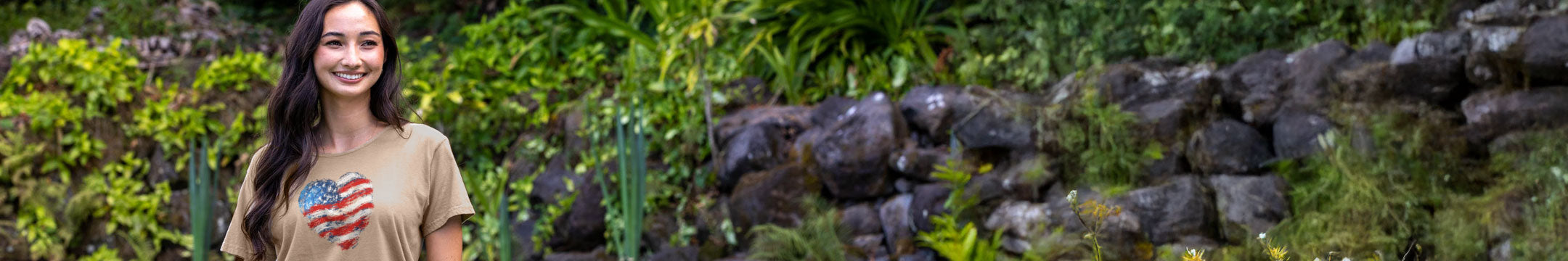 Woman holding a heart-shaped object in front of a stone wall and greenery