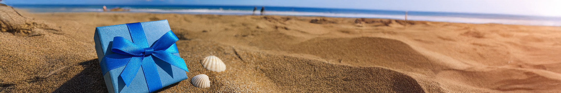 a blue gift box with a bow in the sand on the beach