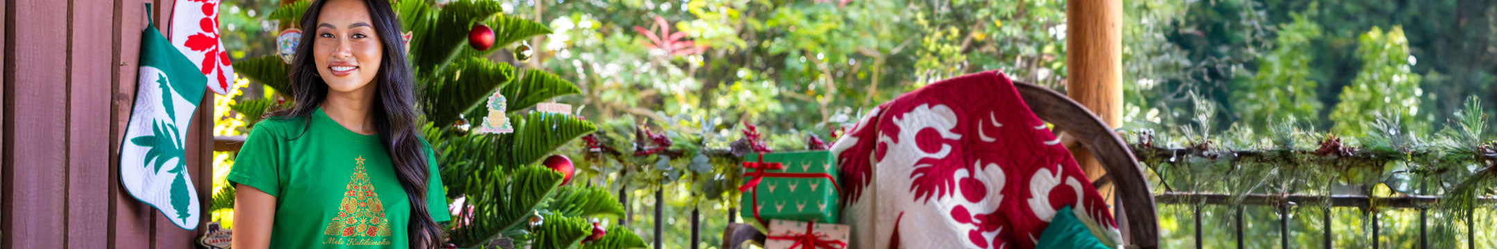 Woman in green shirt with Christmas tree design standing next to a decorated Christmas tree on a porch.