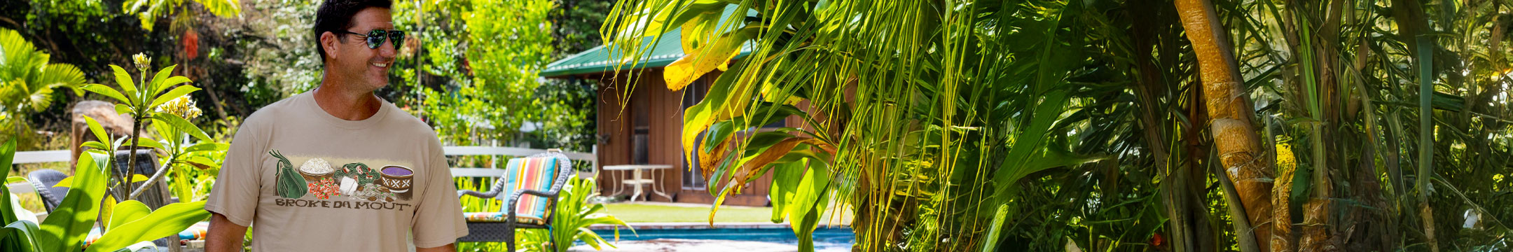 Person standing in a tropical setting with lush greenery and a pool in the background