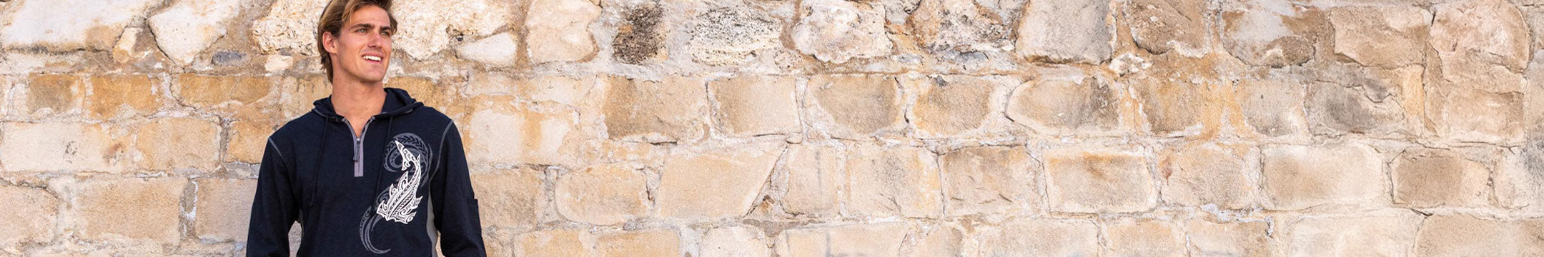 Person wearing a dark hoodie with a graphic design against a stone wall.