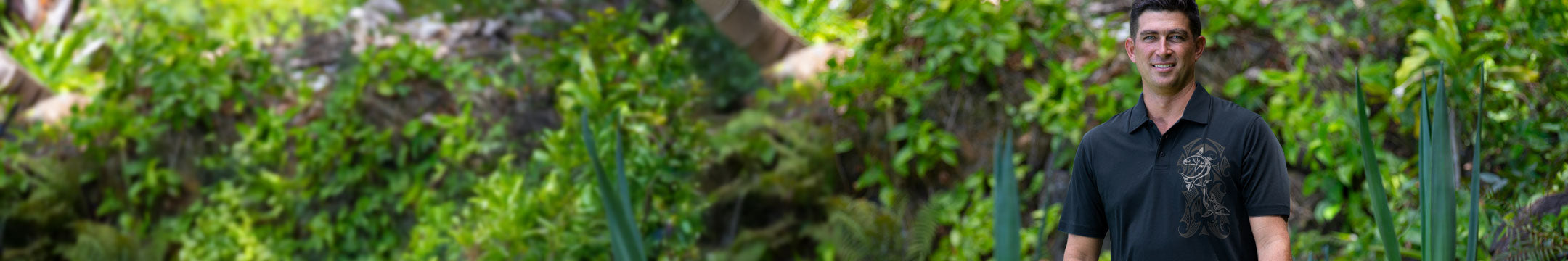 man standing in front of greenery wearing a black collared shirt
