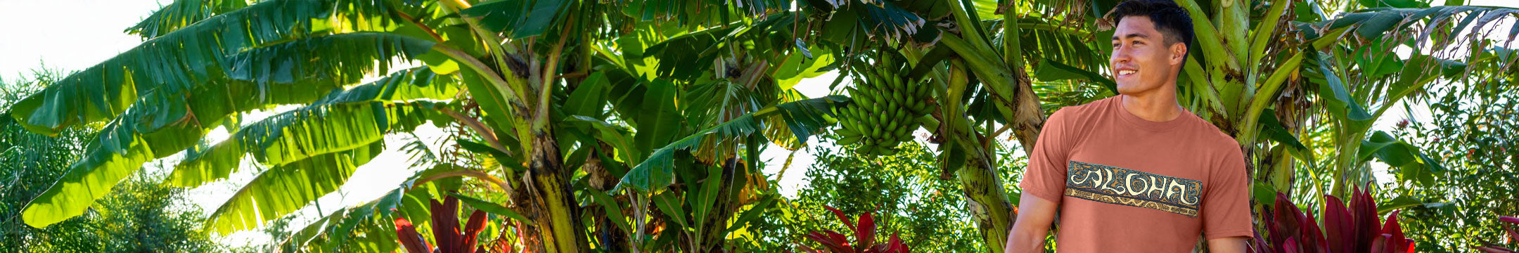 Man standing among banana trees with a 'LOLA' shirt on