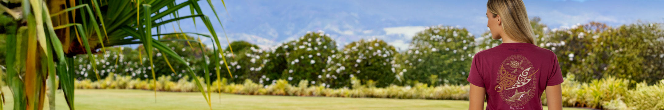 Woman in a maroon t-shirt standing in a park with trees and greenery