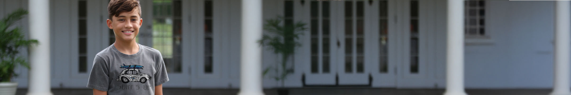 Young boy standing in front of a white house with columns
