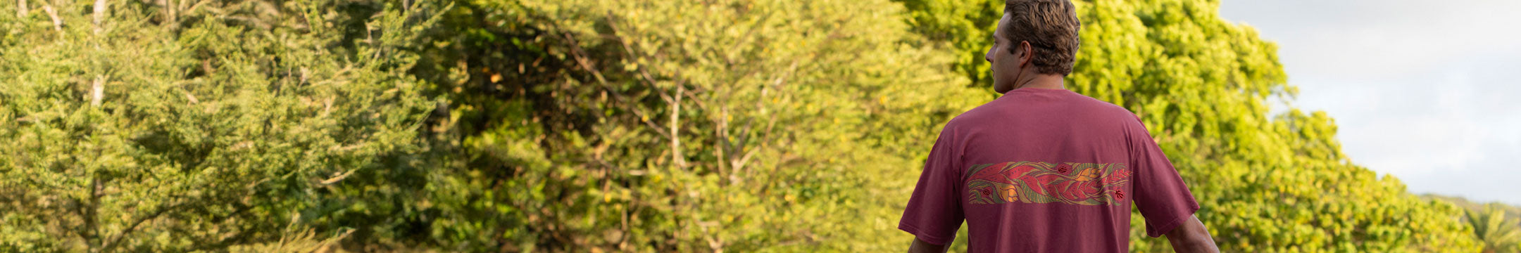 Person wearing a maroon shirt with text standing in a forest