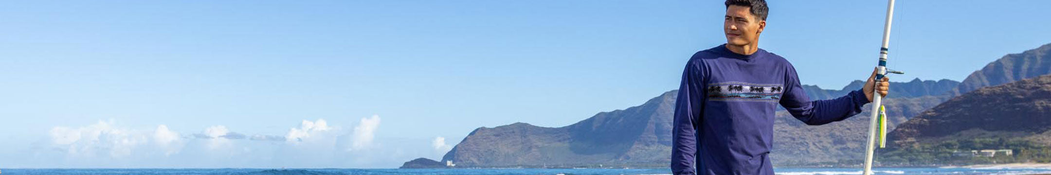 Man holding a fishing rod on a beach with mountains in the background