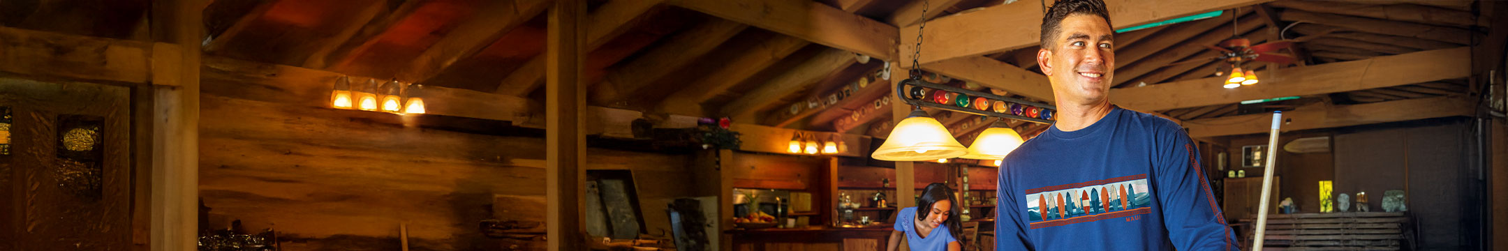Man in a blue long-sleeved shirt standing in a rustic indoor setting with wooden walls and decor.