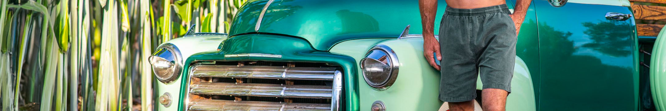 Person standing next to a vintage green truck wearing Pine Dyed shorts 