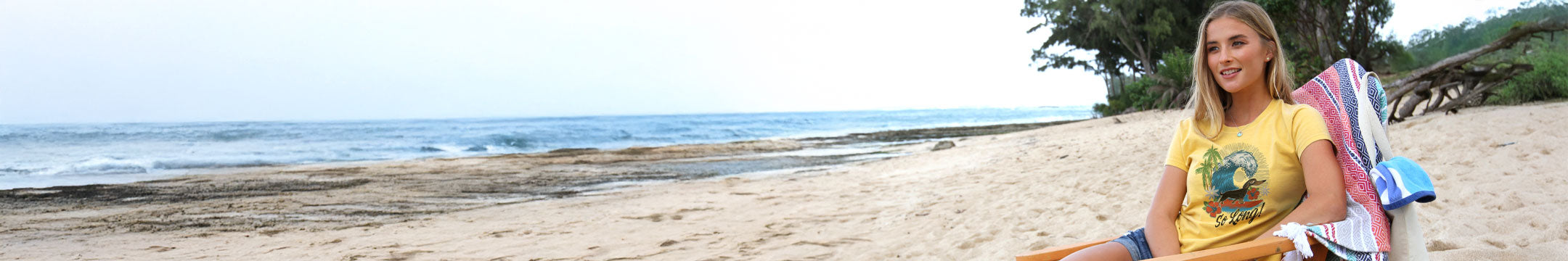 Woman sitting on a beach with a scenic ocean view wearing a Pineapple Dyed Crazyshirt