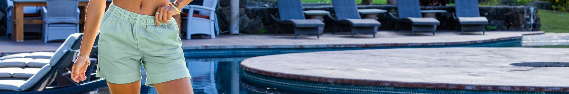 Person wearing light green shorts by a poolside with lounge chairs in the background