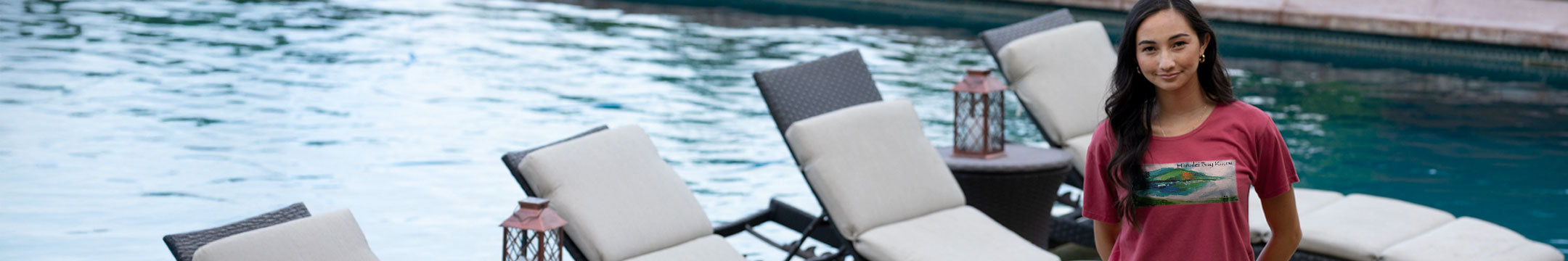 Woman standing by a pool with lounge chairs and a table.