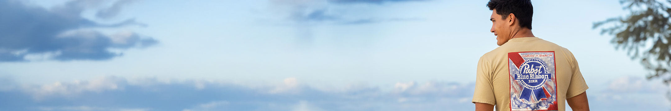 Person wearing a t-shirt with a colorful design, standing against a blue sky.